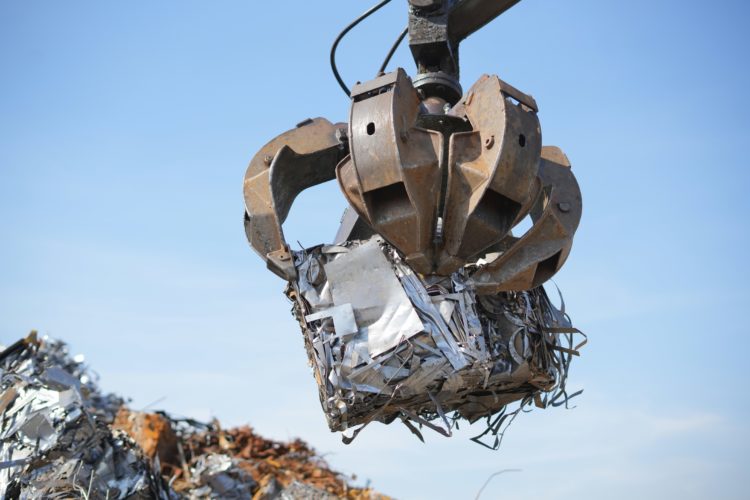 Pince de manutention transportant un cube de déchets métalliques compressés sur site de recyclage